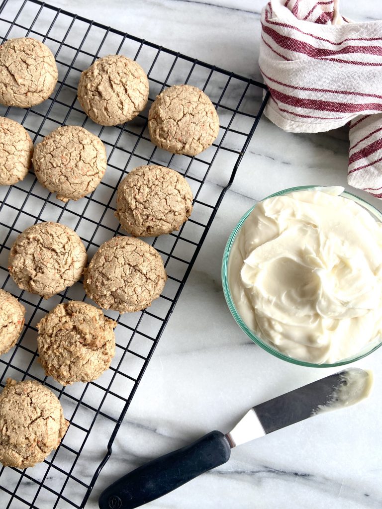 carrot cake cookies on a cooling rack with cream cheese frosting next to them