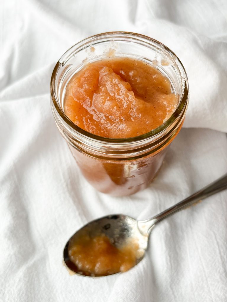 Jar of homemade applesauce on a white background with a spoon in front of the jar