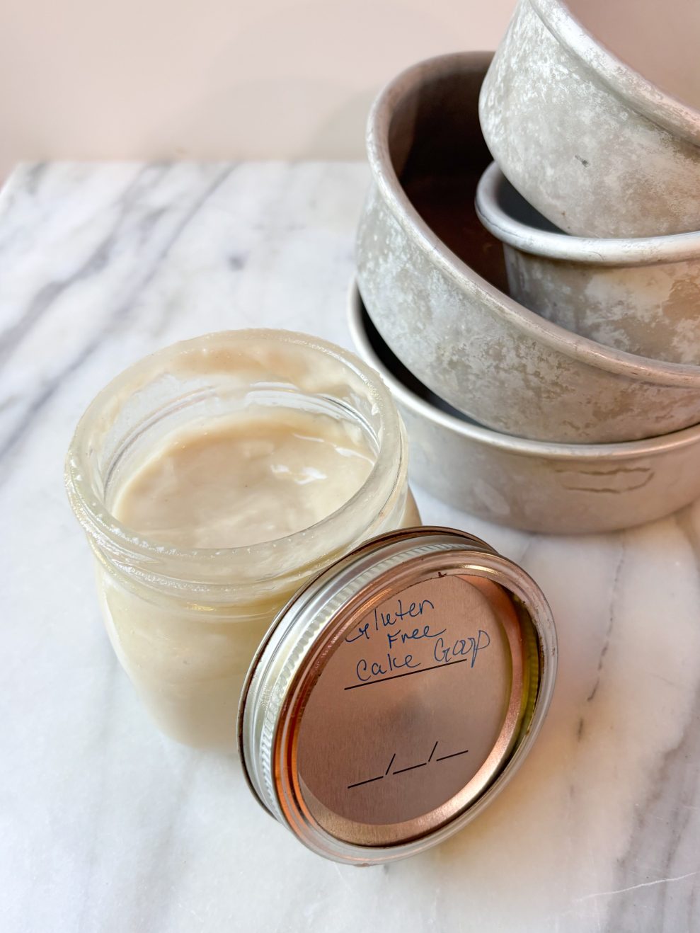 jar of gluten free cake release sitting on a marble counter with cake pans in the background
