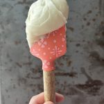 Cream cheese frosting on a pink spatula held up against a gray background