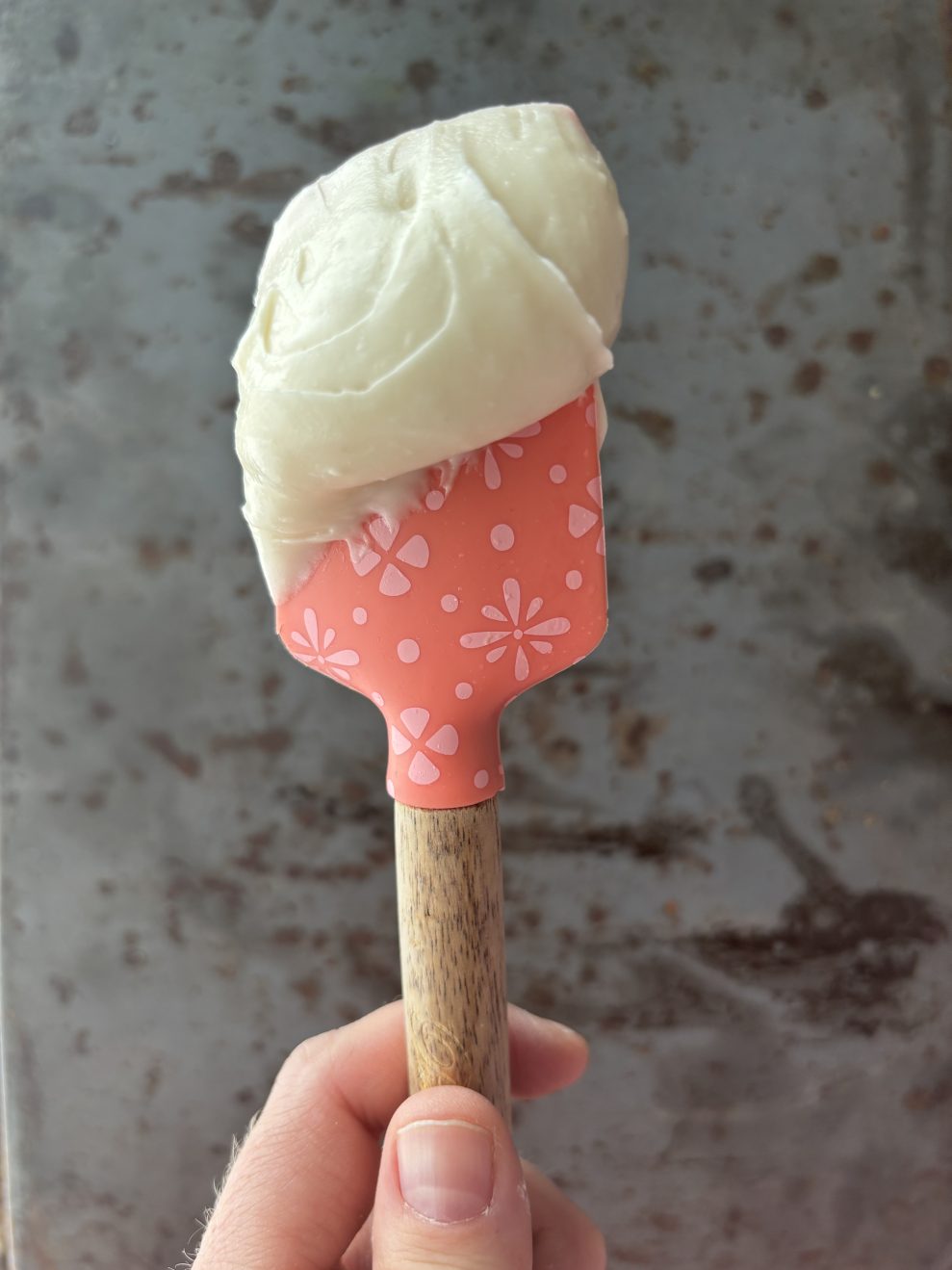 Cream cheese frosting on a pink spatula held up against a gray background