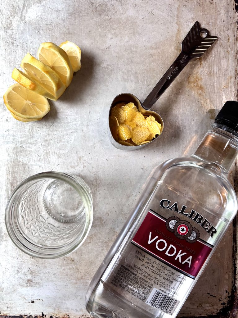ingredients for lemon extract laid out on a pan. Lemon peel, vodka, clean jar